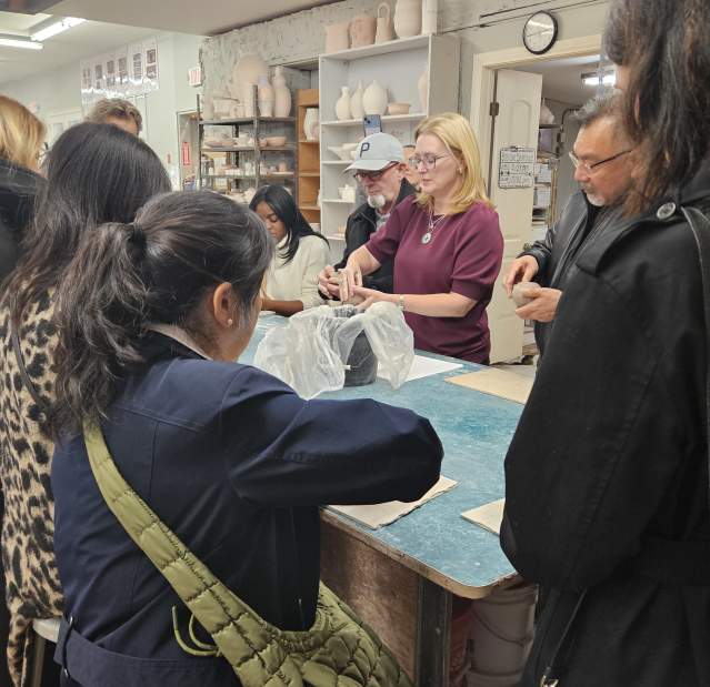 A group of people are gathered around a table working on making pinch pots with clay.