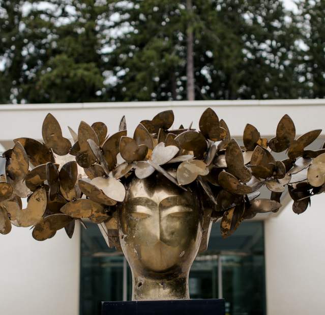 A bronze sculpture of a person's head adorned with a wreath of butterflies on display outside the Katonah Museum of Art.