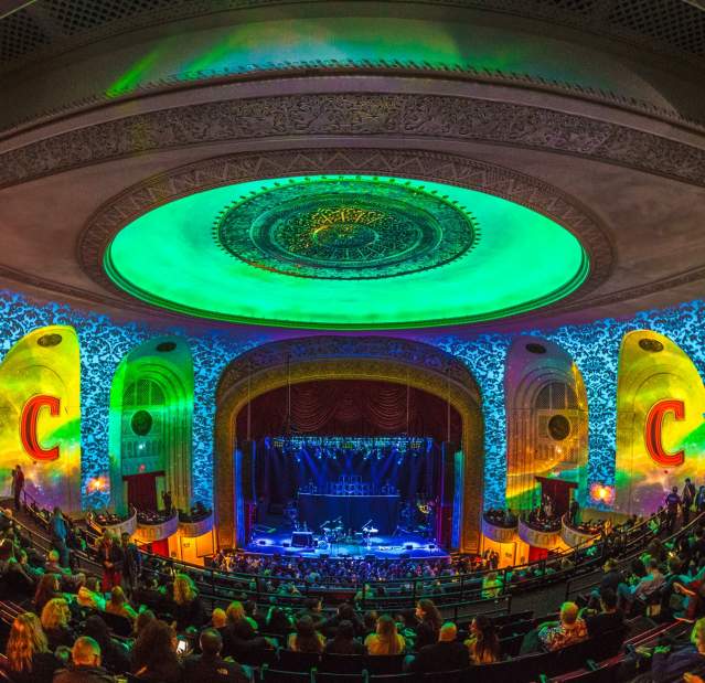 A crowd is gathered for a concert inside The Capitol Theatre. The room is awash in green and yellow lighting.
