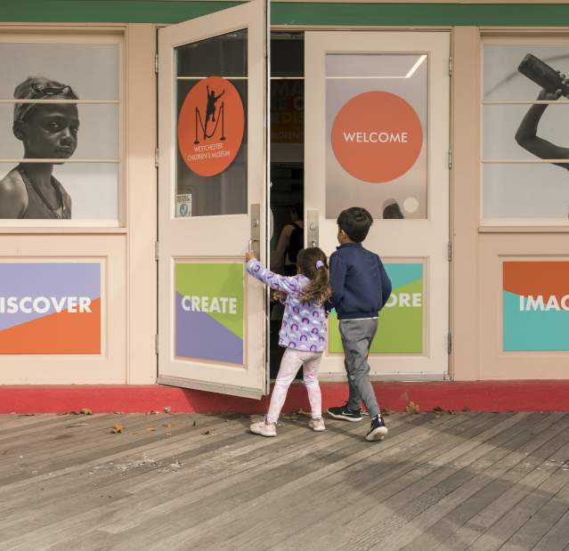 Two children are opening the door of the Westchester Children's Museum.