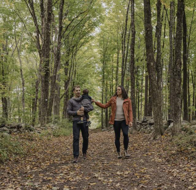 A family with two adults and one child walks down a leafy trail at Ward Pound Ridge Park.