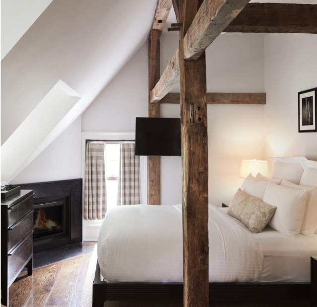 A guest room at the Bedford Post Inn. The room has wooden beams going over the bed and a fireplace can be seen in the background.