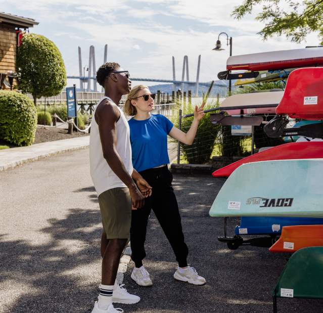 Two people stand next to a group of kayaking, getting ready to choose one and go out on the Hudson River.