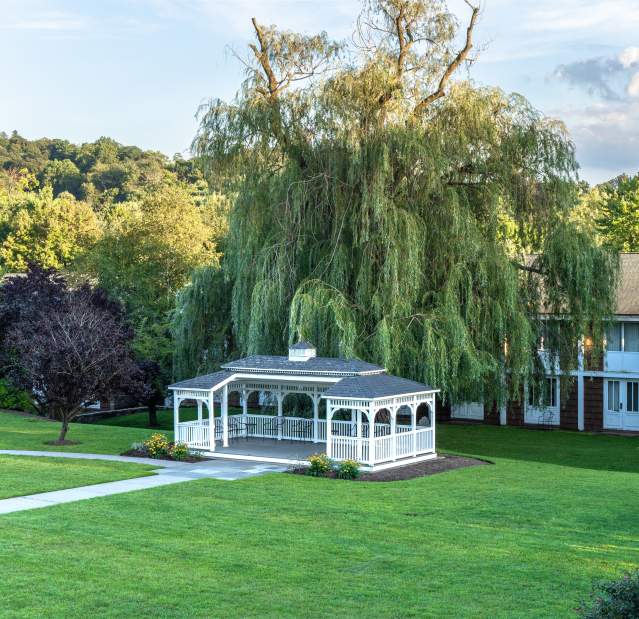 A pavilion with a pathway leading toward it; lush grass surrounds the pavilion.