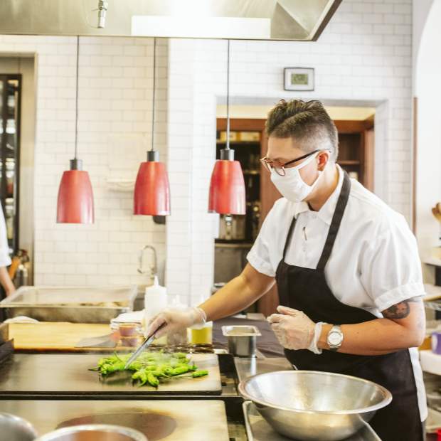 A chef cooks in the kitchen of a restaurant while wearing a mask
