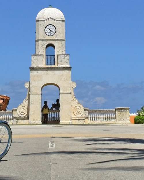 A woman on a blue bike pedaling down a cul de sac in Palm Beach on a clear day
