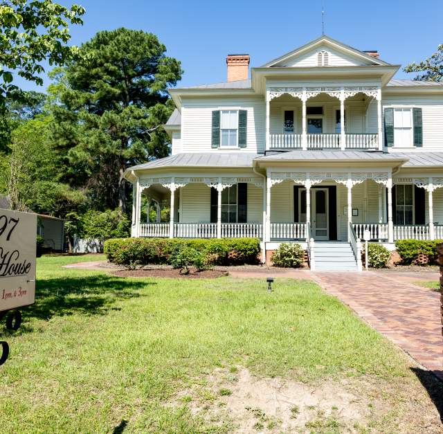 Front view of the historic 1897 Poe House in Fayetteville, North Carolina, surrounded by greenery and featuring its signature wraparound porch and ornate trim.