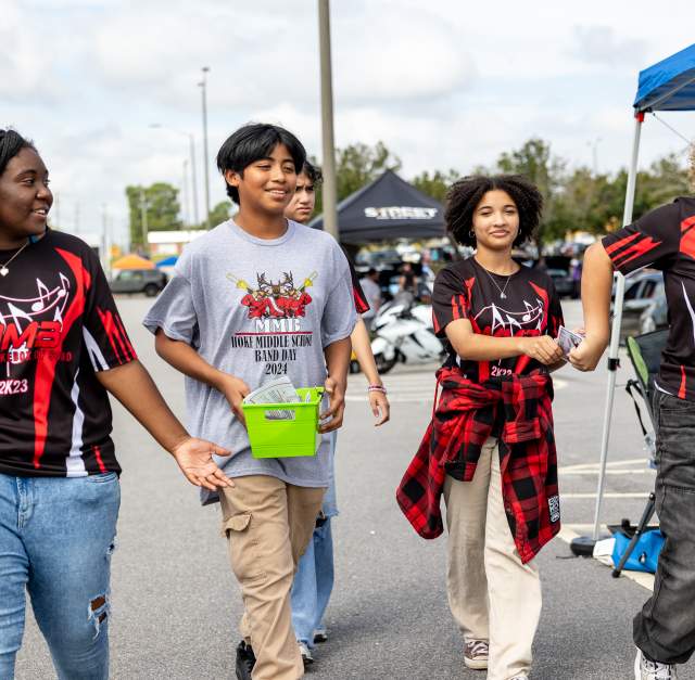 Teens and tweens walk together in matching marching band shirts at an outdoor event in Cumberland County, NC, smiling and chatting in the sunshine.