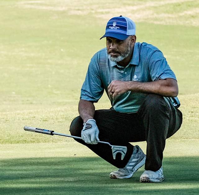 Golfer in a blue shirt and cap crouching on the green while lining up a putt at a local golf course in Cumberland County, NC.