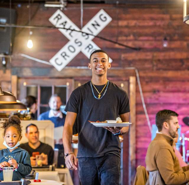 Male server at a restaurant walking holding a plate of food