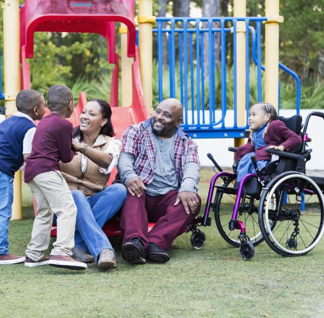 Kids, mother, father and wheelchair-bound child at an outdoor playground