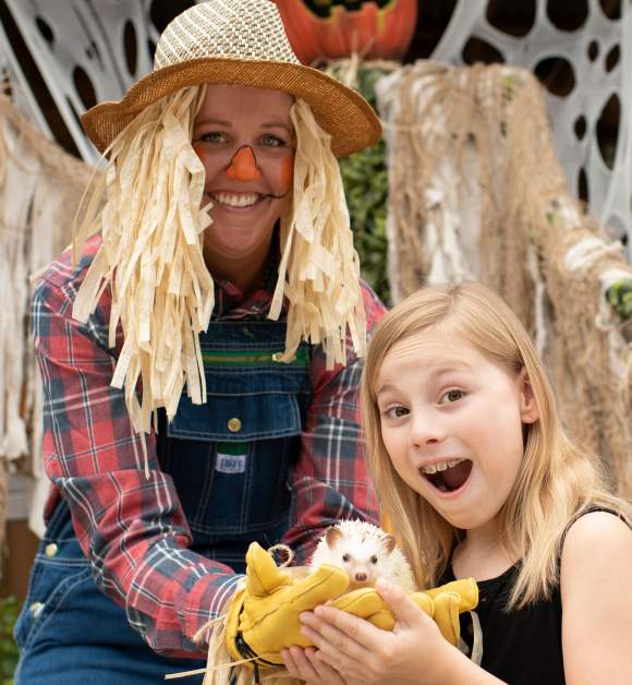 A scarecrow and young girl holding a hedgehog at Gatorland's Gators, Ghosts and Goblins Halloween event.