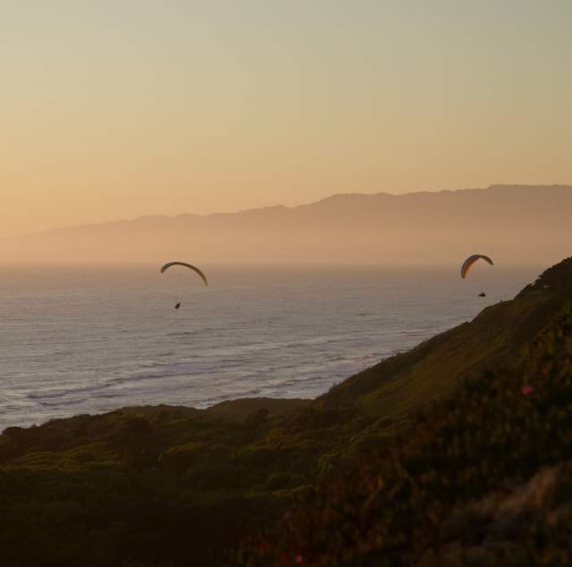 Two paragliders in the air over Thornston State Beach during sunset