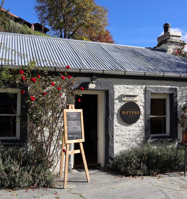 The outside of a white brick cottage with signs out the front for gin tasting