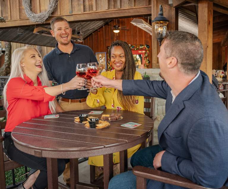 Four friends share laughter and raise their wine glasses in a cheerful toast at Duplin Winery, festively decorated, creating a warm and joyful holiday atmosphere.