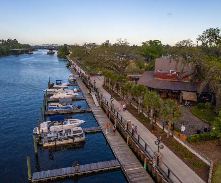 Scenic aerial view of the Barefoot Landing marina and boardwalk along the Intracoastal Waterway in North Myrtle Beach, South Carolina, with docked boats, palm trees, and waterfront dining.