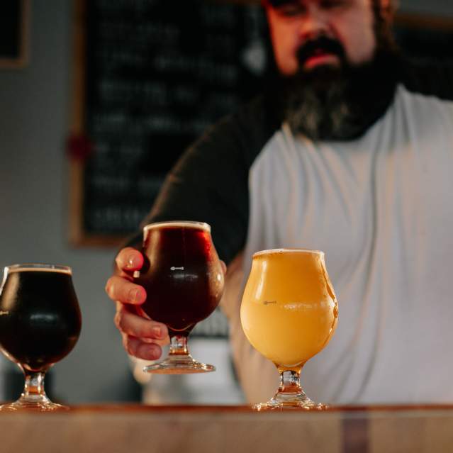A bartender sets down a glass of beer in a beer flight featuring a dark beer, amber beer, and wheat beer.