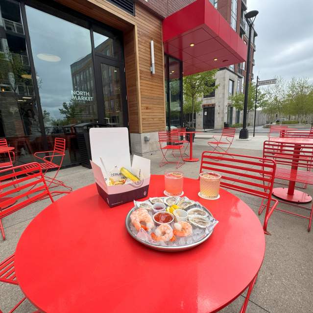 A tray of shrimp and oysters on a red metal table surround by red chairs on the patio of Market Bar at North Market Bridge Park.