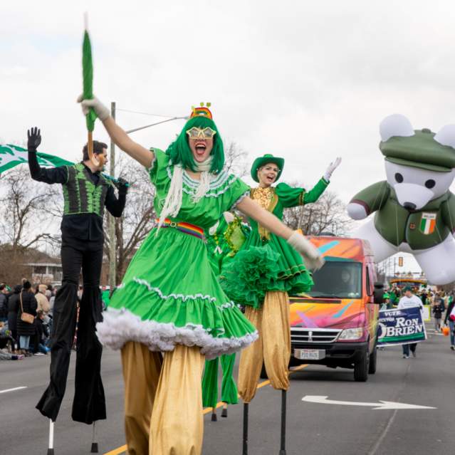 A group of stilt walkers dressed in green performing down the street in the St. Patrick's Day Parade.