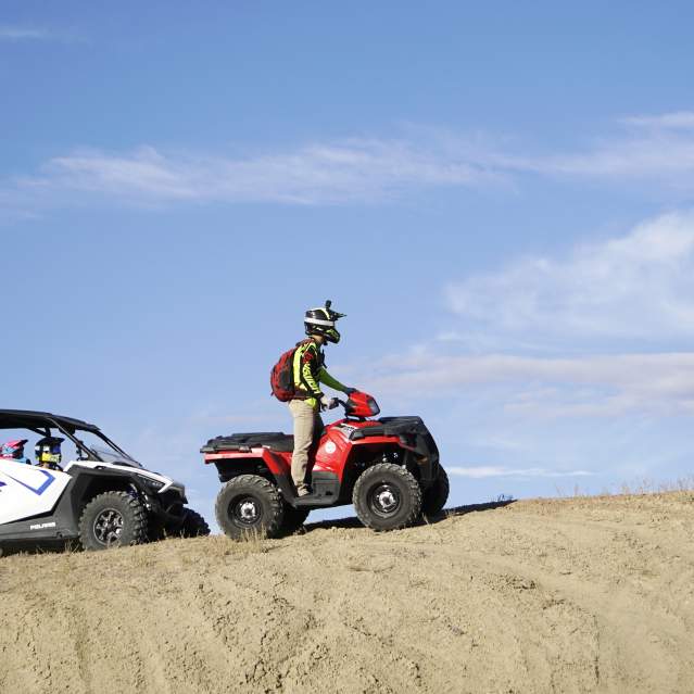 Dirtbiker jumping while people on a fourwheeler and RZR watch