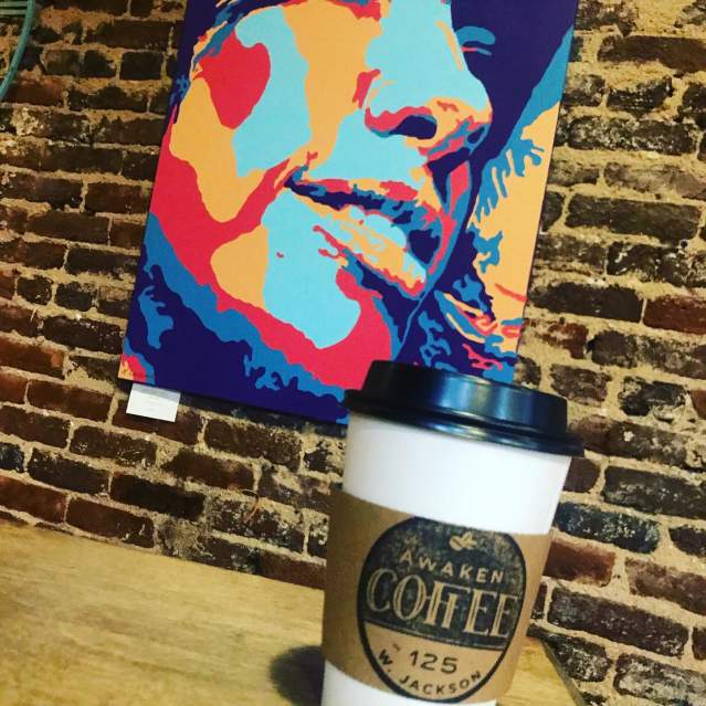 A brightly-colored painting decorates the wall behind a fresh cup from Awaken Coffee.