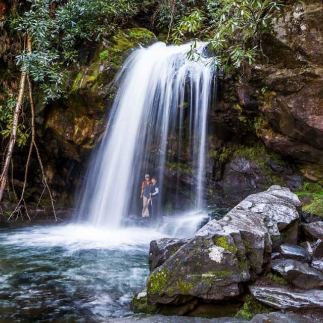 Hikers standing under the Grotto Falls on Trillium Gap Trail near Knoxville