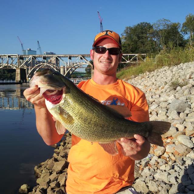 Man holding small mouth bass on shore of Tennessee River