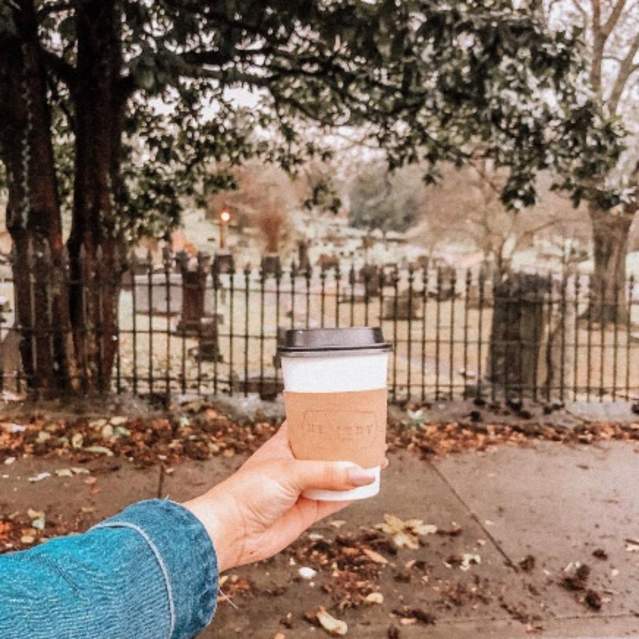 A visitor to Remedy Coffee shows off their fresh cup of morning joe on an autumn day.