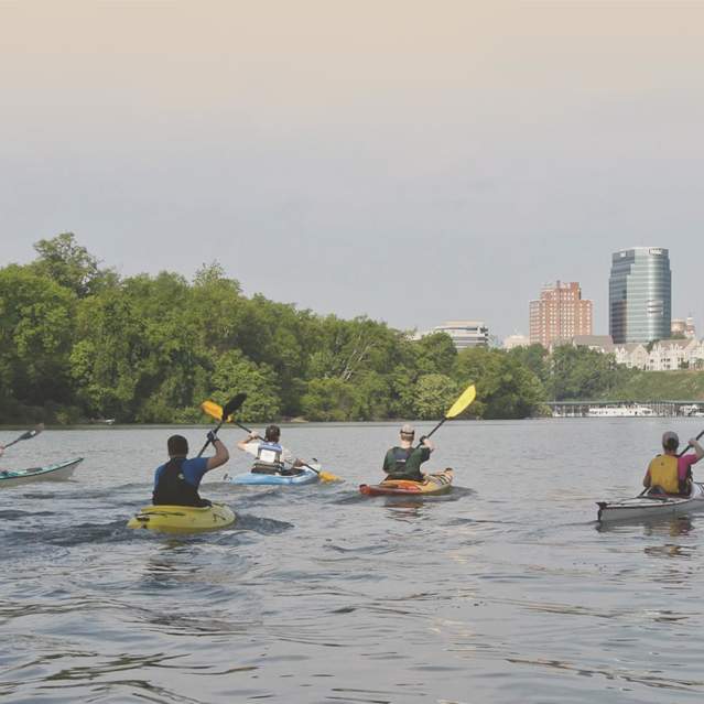 Kayakers paddle down a river with a view of downtown Knoxville, TN