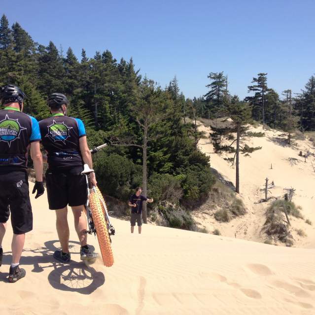 Two cyclists with a fat tire bike look over the sand dunes.