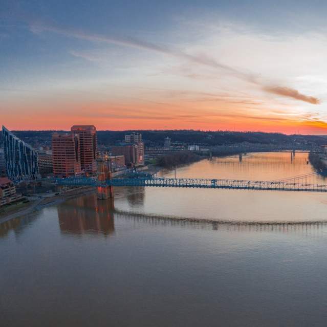 Orange and pink sunset behind the Roebling suspension bridge, the Ohio river, the Ascent and the rest of the Northern Kentucky skyline