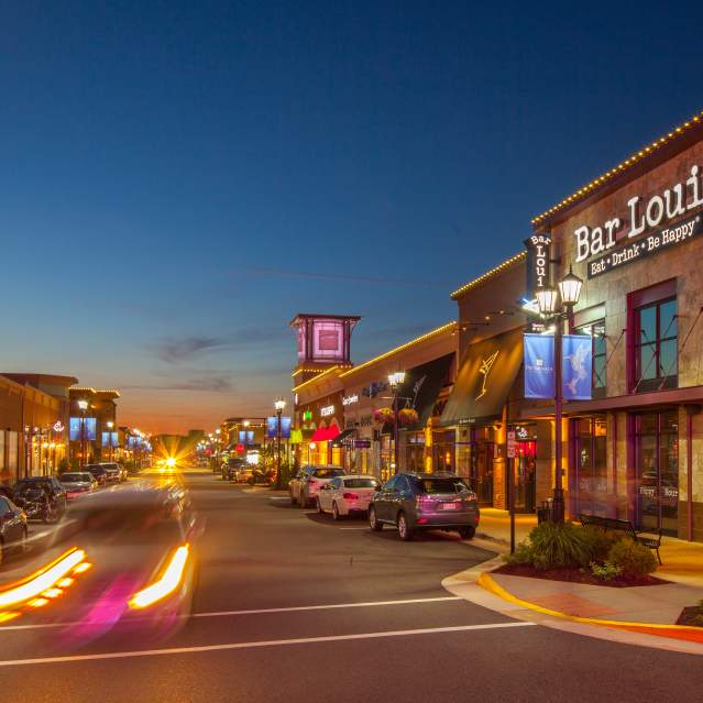 a shopping area with cars going by at night