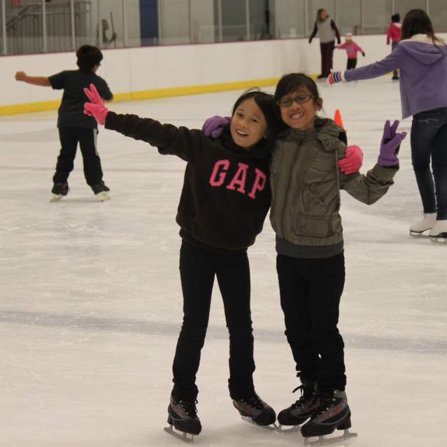 Two girls hugging and holding up peace signs at an ice skating rink