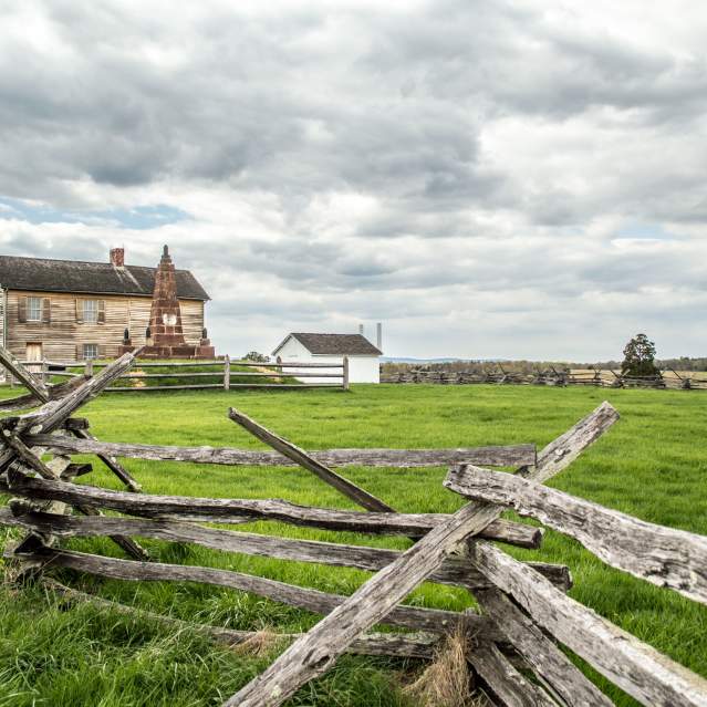 A battlefield with a wooden fence and a historic building in the background