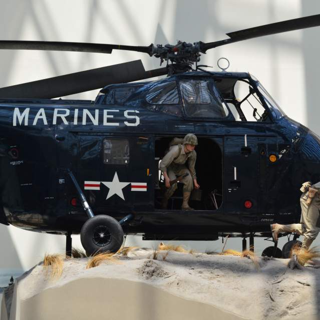 a navy helicopter with the word "marines" on the front with 2 statues of men coming out of the helicopter