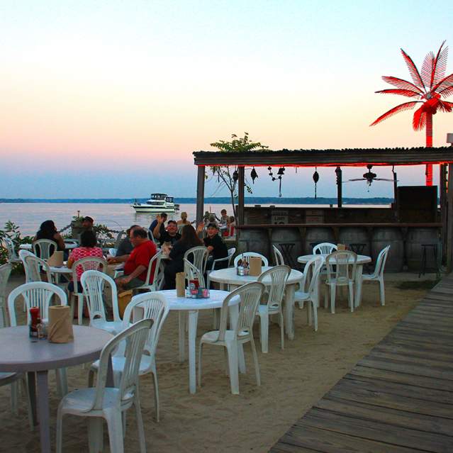 tables and chairs on a beach at sunset