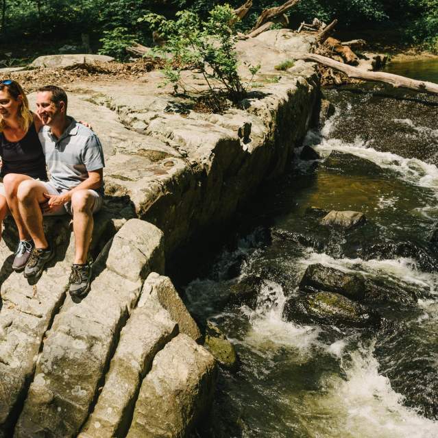 a couple sitting on the edge of a rock near water