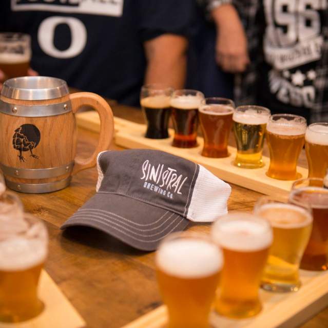 A hat with the Sinistral Brewing Co logo surrounded by flights of beer