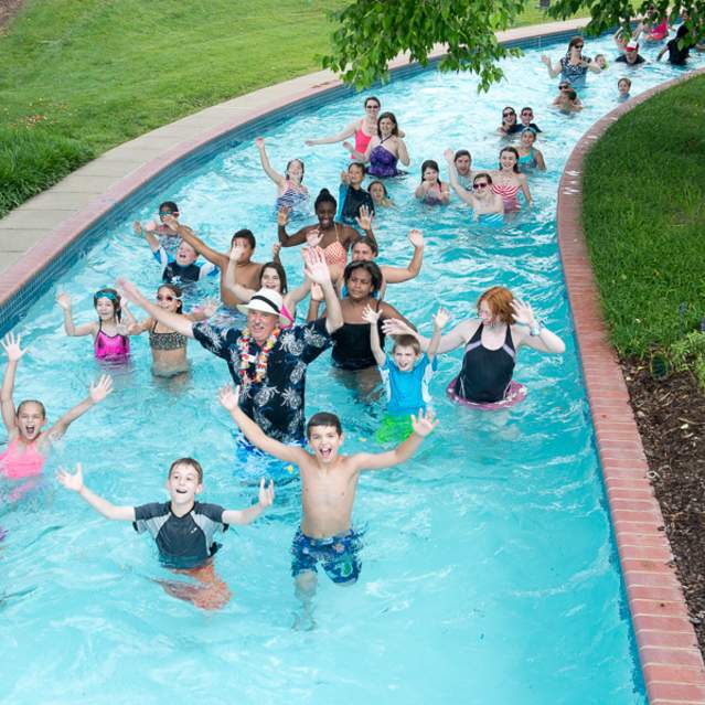People of all ages in a lazy river with their hands up smiling