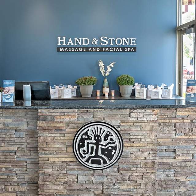 a desk at a salon, the desk has a stonefront, the wall in the back is blue and says "Hand & Stone Massage and Facial Spa"