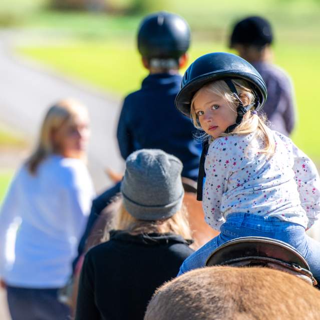 Young white girl looking over her shoulder on a horse being lead by an instructor