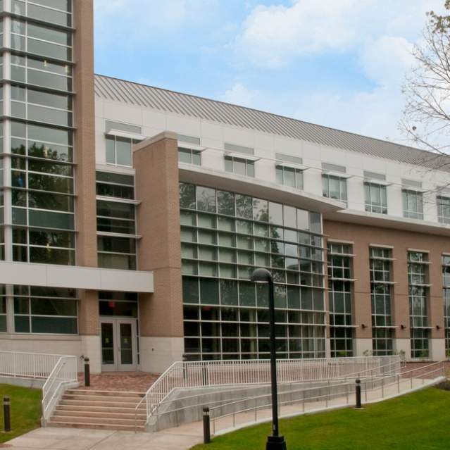 a brick building with many windows, a walking area, stairs and trees