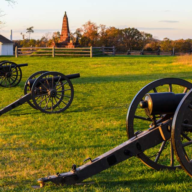 Three cannons on a battlefield with a historic house in the background