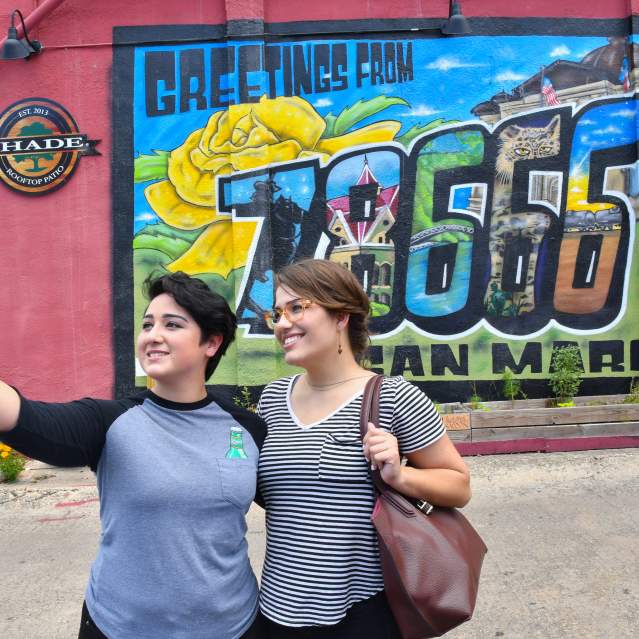 Couple takes a selfie in front of the Greetings from 78666 mural in Kissing Alley in downtown San Marcos.
