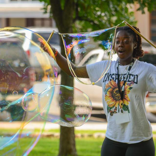 a girl outside marveling at a giant bubble she is making at the bubble bash event