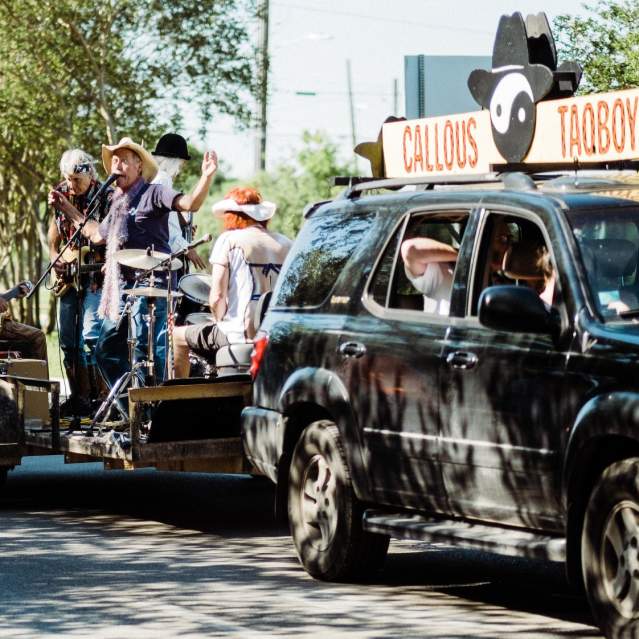 A band playing on a flat bed trailer being pulled by SUV