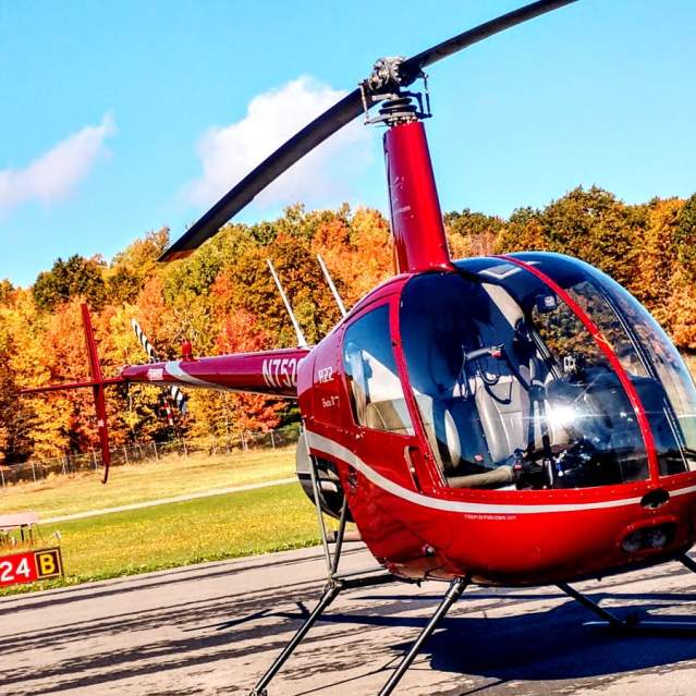 Red helicopter on the ground with fall foliage in the background