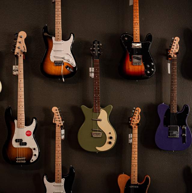 A variety of electric guitars are hanging on a dark gray wall.