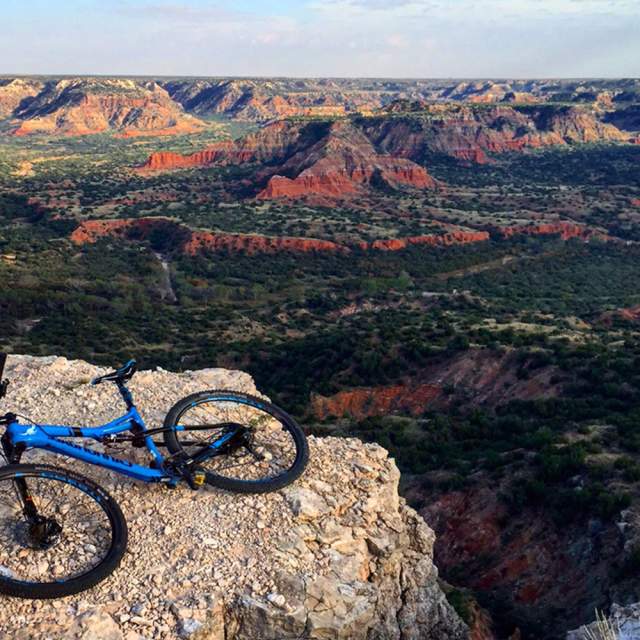 mountain bike laying on top of a cliff overlooking palo duro canyon