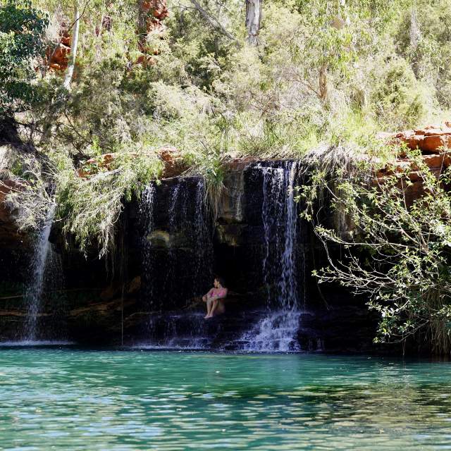 A woman sitting under the waterfall at Fern Pool in Karijini National Park